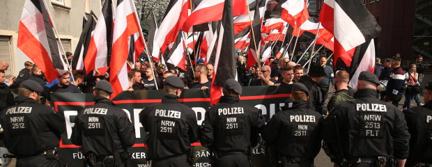 Polizisten stehen vor fahnenschwenkenden Demonstranten bei einer Demonstration von Rechtsextremisten.