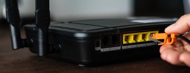Hand steckt LAN-Kabel in schwarzen Router