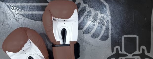 Braune Boxhandschuhe auf grauem Betonboden. Schemenhafter Reichsadler auf Boden. Braune Boxhandschuhe auf grauem Betonboden. Schemenhafter Reichsadler auf Boden.