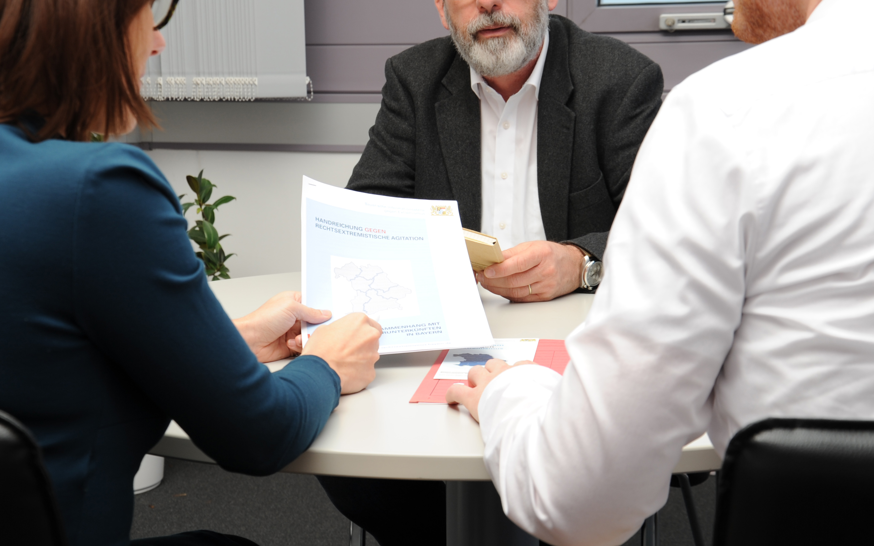Drei Personen sitzen an einem Tisch zusammen im Rahmen einer Beratung zu Extremismus der Bayerischen Informationsstelle gegen Extremismus (BIGE).