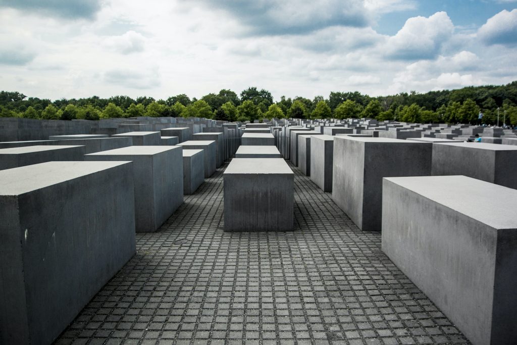 Schwarze Stelen des Denkmals für die ermordeten Juden Europas (Holocaust-Denkmal) in Berlin mit Bäumen im Hintergrund und bewölktem Himmel.