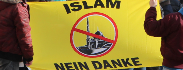 Aktivisten des extremistischen Phänomenbereichs Verfassungsschutzrelevante Islamfeindlichkeit zeigen auf einer Kundgebung ein gelbes Banner mit der Aufschrift "Islam nein danke" und einer durchgestrichenen Moschee.