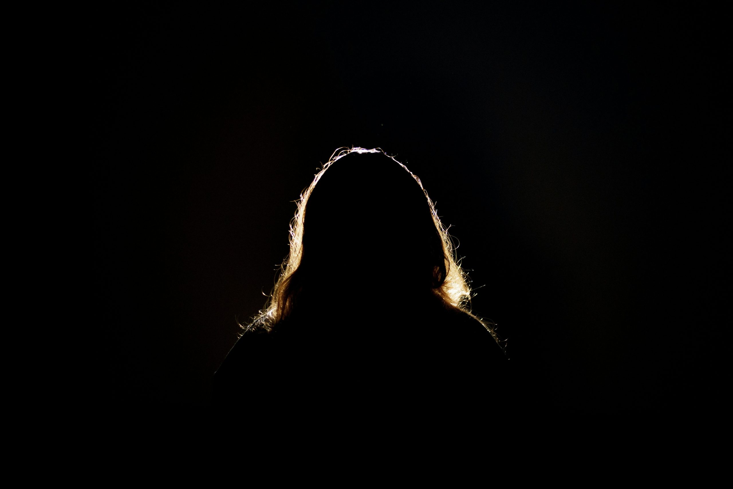 Eine Frau mit langen Haaren, die im Dunkeln steht, Gesicht nicht zu erkennen.