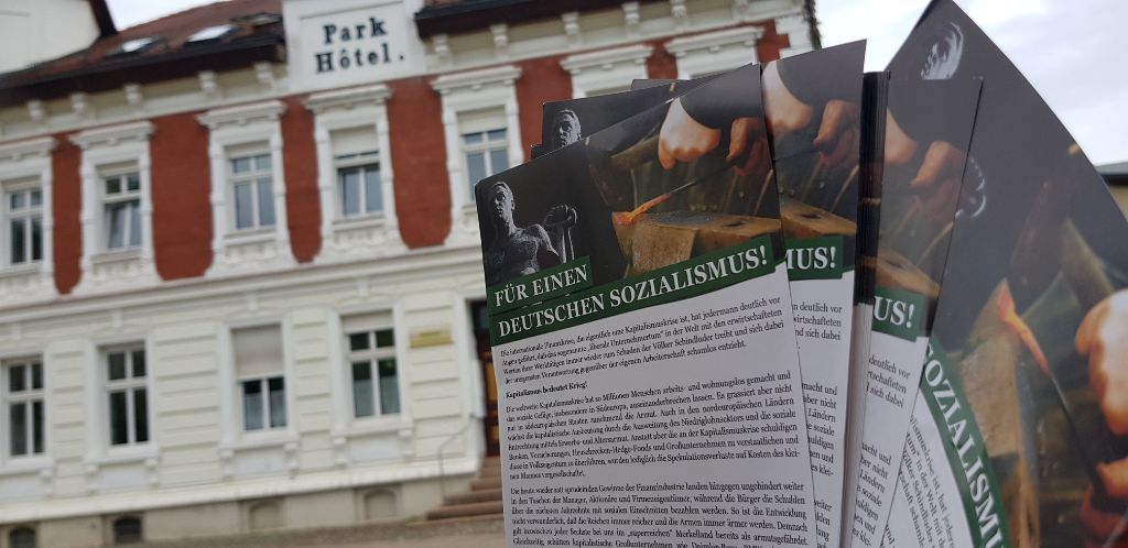 Info-Flyer der neonazistischen Kleinpartei Der Dritte Weg werden vor einem Gebäude hochgehalten.