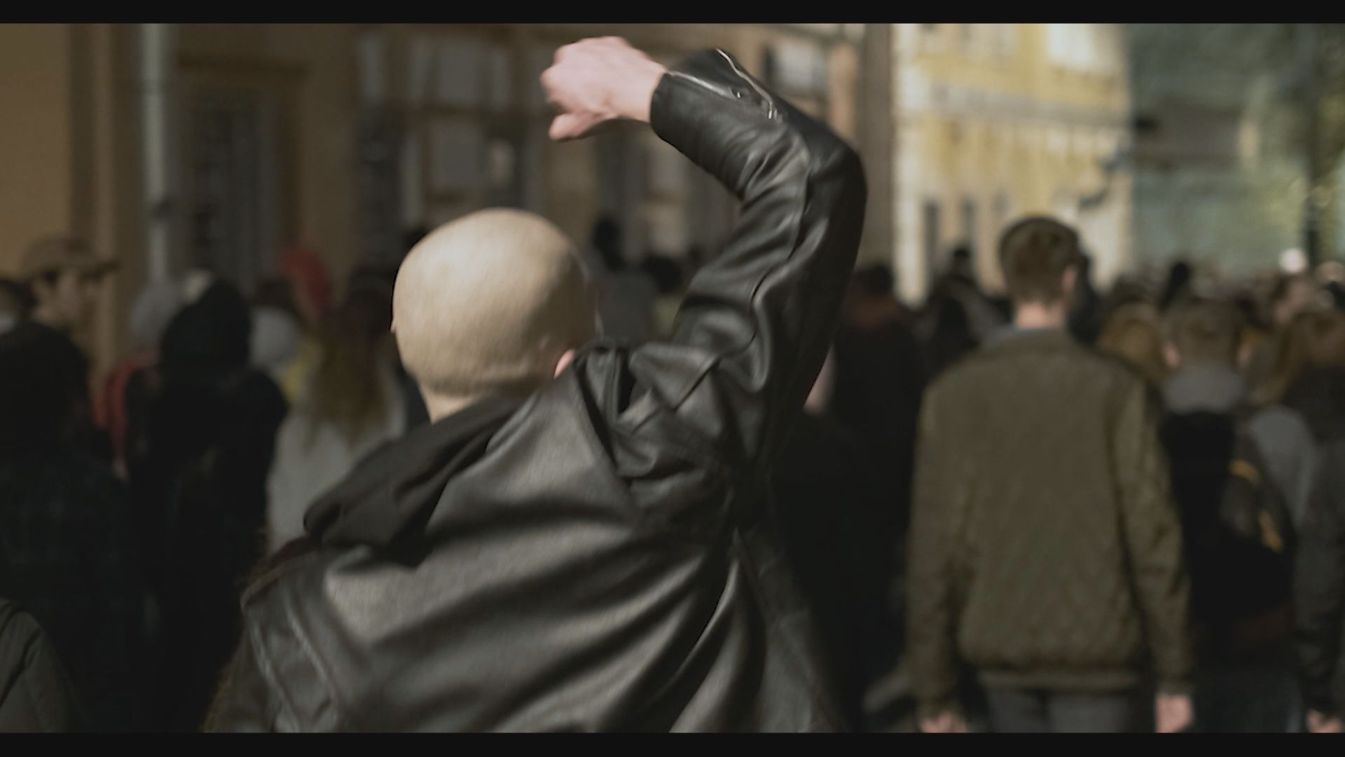 Skinhead mit schwarzer Lederjacke von hinten betrachtet auf einer Demonstration den rechten Arm mit Faust nach oben erhoben