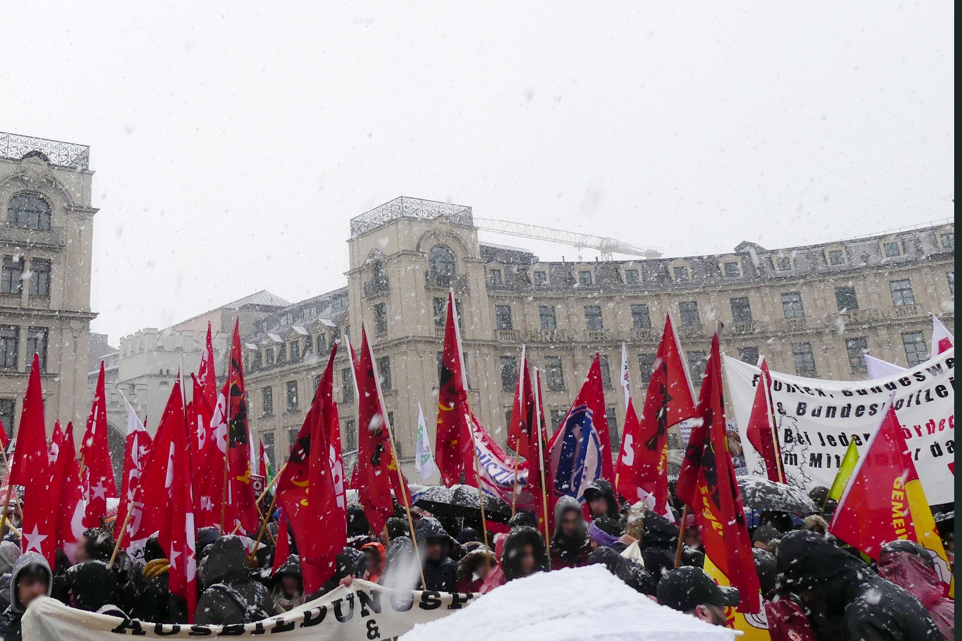 Teilnehmer einer linksextremistischen Demonstration halten Banner und rote Fahnen in die Höhe im Schneegestöber in der Münchner Innenstadt.