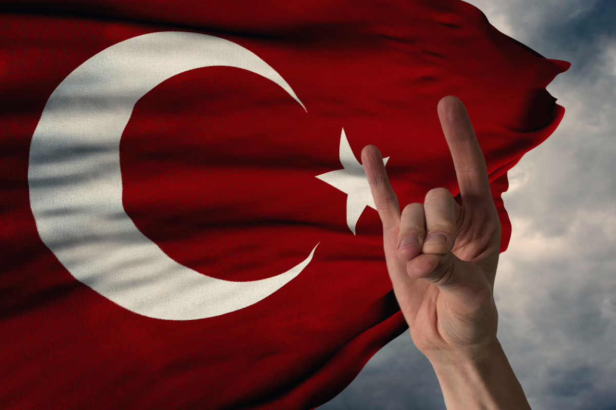 Eine Hand zeigt den Wolfsgruß türkischer Rechtsextremisten der Ülkücü-Bewegung vor einer wehenden Flagge der Türkei.